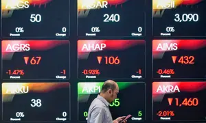 Seorang pria melihat ponselnya di depan layar yang menampilkan Indeks Harga Saham Gabungan (IHSG), yang anjlok signifikan selama pembukaan pasar, di gedung Bursa Efek Indonesia di Jakarta pada Rabu 13 Mei 2026. (BAY ISMOYO/AFP)