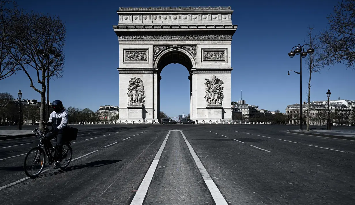 Seorang pria mengendarai sepedanya melewati Arc de Triumph selama kebijakan lockdown berlangsung untuk menghentikan penyebaran pandemi virus corona Covid-19 di Paris pada 23 Maret 2020. (Photo by PHILIPPE LOPEZ / AFP)