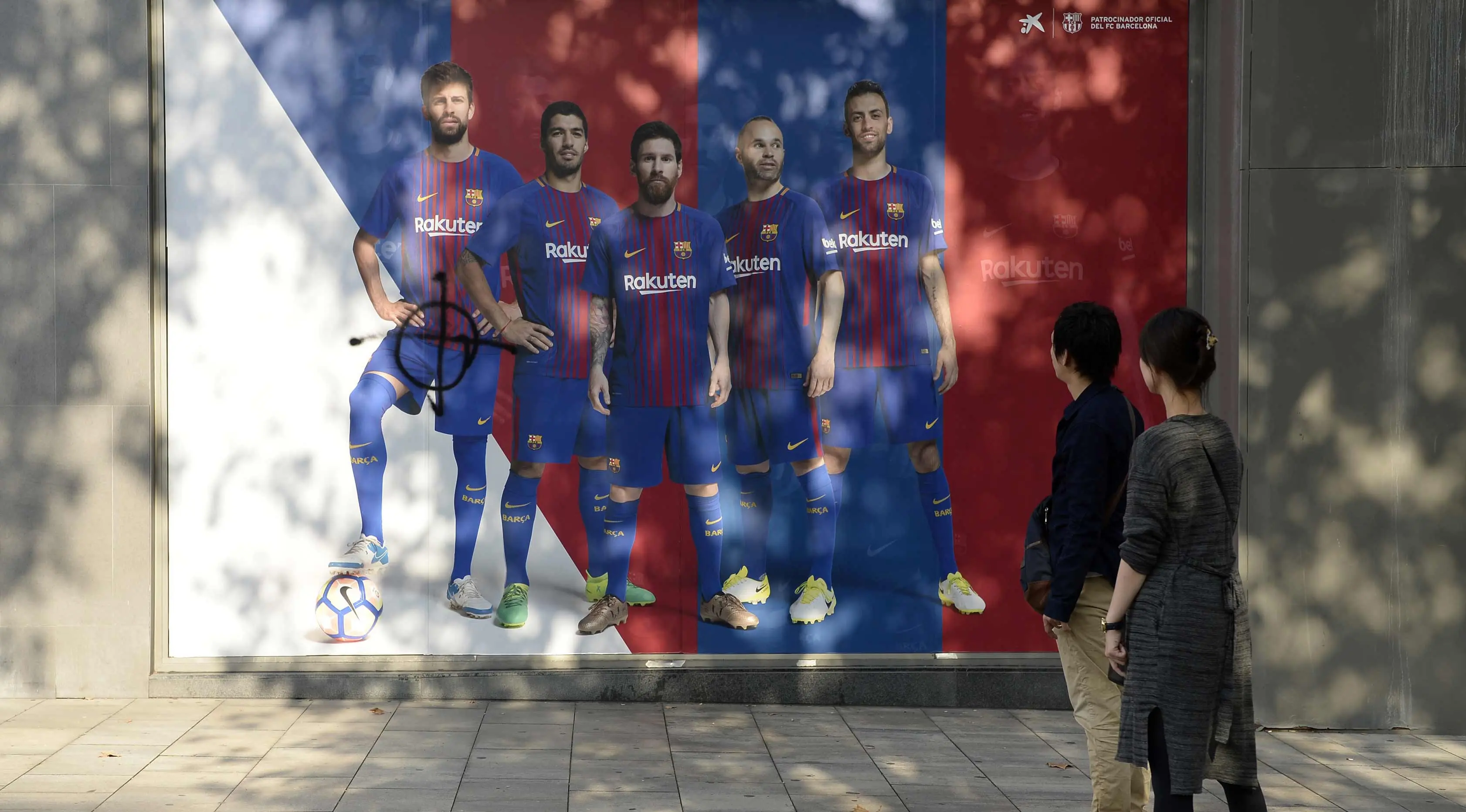 Fans melihat poster pemain Barcelona, Gerard Pique yang dirusak di sebuah toko yang ditutup sebagai bagian dari pemogokan oleh serikat pekerja Catalonia di luar stadion Camp Nou, Barcelona (3/10). (AFP Photo/Josep Lago)