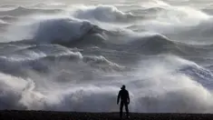 Seseorang melihat ke arah ombak yang menerjang pantai di Newhaven pada tanggal 2 Januari 2024. (ADRIAN DENNIS/AFP)