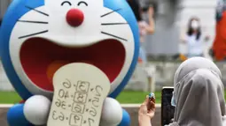Seorang pengunjung memotret patung Doraemon kecil miliknya berlatarkan salah satu patung di pameran "Doraemon's Time-Travelling Adventures in Singapore" yang digelar di Museum Nasional Singapura pada 3 November 2020. Pameran ini akan berlangsung hingga 27 Desember 2020. (Xinhua/Then Chih Wey)