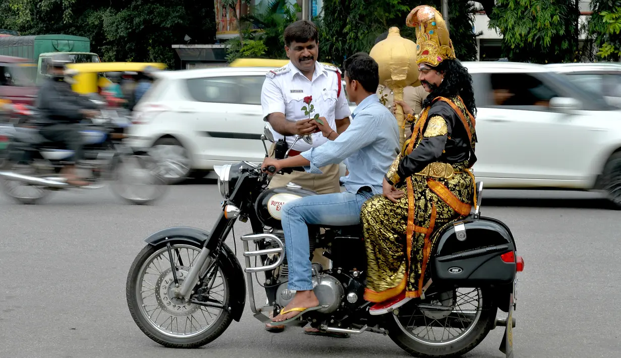 Polisi memberi mawar kepada pengendara motor tanpa helm yang membonceng seniman berpakaian seperti "Yamaraj", dewa kematian Hindu saat  kampanye 'Road Safety Week' di Bangalore (10/7). (AFP Photo/Manjunath Kiran)