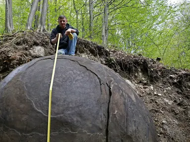 Suad Keserovic mengukur bola batu temuannya di dalam hutan di Desa Podunavlje, Zavidovici, Bosnia dan Herzegovina, Senin (11/4). Pria itu mengklaim bola batu berdiameter 3,30 meter tersebut memiliki berat sekitar 35 ton. (REUTERS/Dado Ruvic)