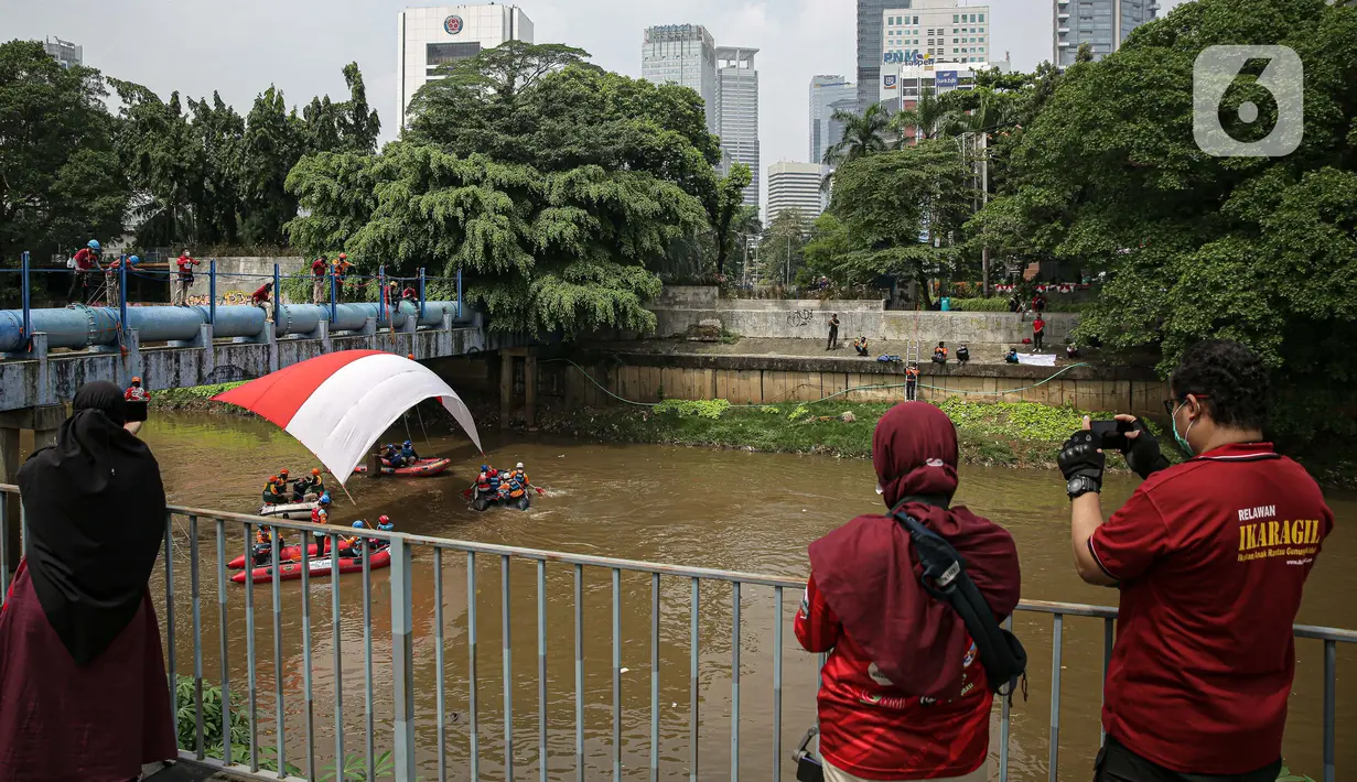 Warga menyaksikan pembentangan bendera Merah Putih di aliran kali
Ciliwung di kawasan Sudirman, Jakarta, Minggu (22/8/2021). Pembentangan atau pengibaran bendera Merah Putih tersebut dilaksanakan untuk memperingati HUT ke-76 RI. (Liputan6.com/Faizal Fanani)