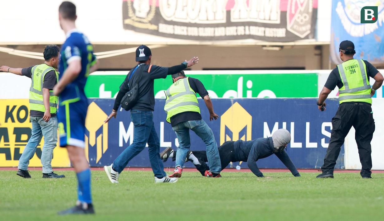 Petugas keamanan berusaha menangkap suporter nakal yang nekat masuk ke lapangan saat Persib Bandung melawan Persik Kediri pada laga BRI Liga 1 2022/2023 di Stadion Pakansari, Bogor, Rabu (8/3/2023). (Bola.com/M Iqbal Ichsan)