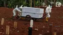 Petugas membawa dua peti jenazah yang akan dimakamkan dengan protokol COVID-19 di TPU Pondok Ranggon, Jakarta, Sabtu (17/10/2020). Petugas terpaksa menggunakan gerobak untuk membawa peti jenazah dikarenakan kondisi tanah yang lengket dan licin akibat diguyur hujan. (Liputan6.com/Helmi Fithriansyah)