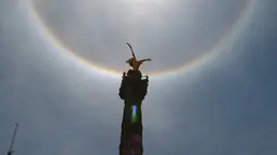 Fenomena halo matahari dengan latar depan monumen Malaikat Kemerdekaan di pusat kota Mexico City, Sabtu (7/7). Fenomena halo matahari terjadi karena pembiasan kristal es yang berada di sekitar Matahari yang membentuk semacam pelangi. (AP/Anthony Vazquez)