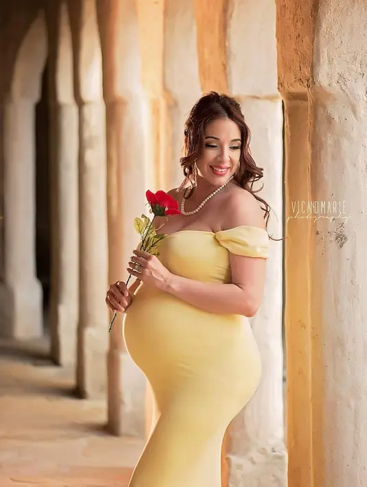 Wanita yang sedang hamil besar ini mengenakan gaun kuning berpose memegang bunga seperti karakter Belle dari film 'Beauty and The Beast'. (Instagram/vicandmariephotography)