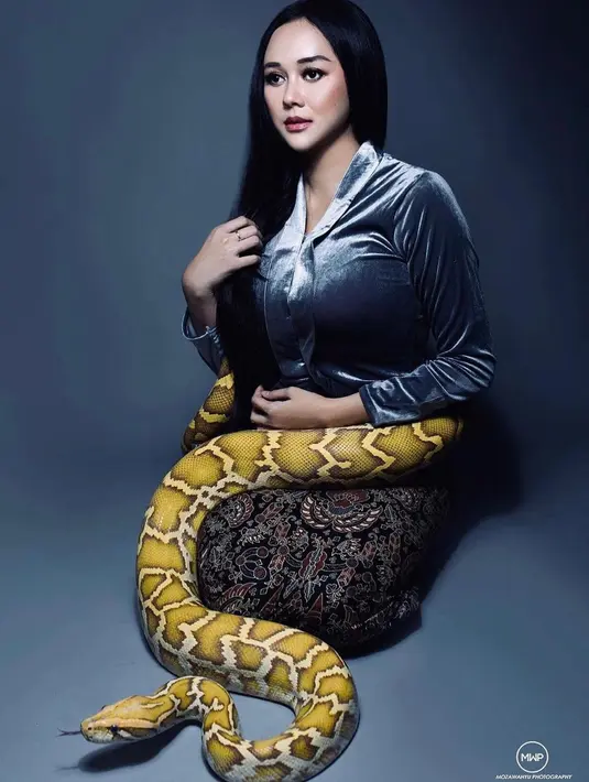 Pemilik nama Sanny Aura Syahrani itu terlihat mengunggah sesi pemotretan dirinya bersama seekor ular jenis phyton. Ibu satu anak itu memamerkan foto dirinya sedang bersimpuh mengenakan kain dan kebaya sambil menunjukkan tatapan mata kosong. Di tubuhnya, terlihat ular phyton besar berwarna albino sedang melingkar. (Liputan6.com/IG/@aurakasih)