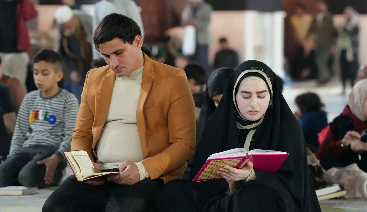 Memperbanyak bacaan Al Quran di akhir bulan merupakan bentuk konsistensi dalam beribadah juga sebagai bagian dari menghidupkan malam 10 malam terakhir Ramadan. Tampak dalam foto, seorang pria dan wanita Muslim Syiah membaca Al-Quran, membaca Al-Quran, saat melaksanakan Itikaf di Masjid Kufa, selatan Baghdad, Irak, pada 12 Maret 2026. (Qassem al-KAABI/AFP)