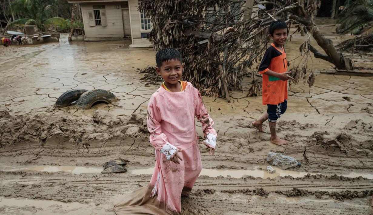 Sementara, Desa Babo merupakan sebuah kampung yang terletak di Kecamatan Bandar Pusaka, Kabupaten Aceh Tamiang, Provinsi Aceh. Tampak dalam foto, seorang anak laki-laki mengenakan pakaian sumbangan berjalan di sepanjang jalan berlumpur di Babo, Aceh Tamiang, pada Senin 15 Desember 2025. (Yasuyoshi CHIBA/AFP)