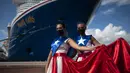 Ivanelis Jimenez (depan) dan Veronica Barreto mengenakan gaun bendera Puerto Rico saat menyambut penumpang kapal pesiar Mardi Gras Carnival yang berlabuh di Teluk San Juan, Puerto Rico, Selasa (3/8/2021). (AP Photo/Carlos Giusti)