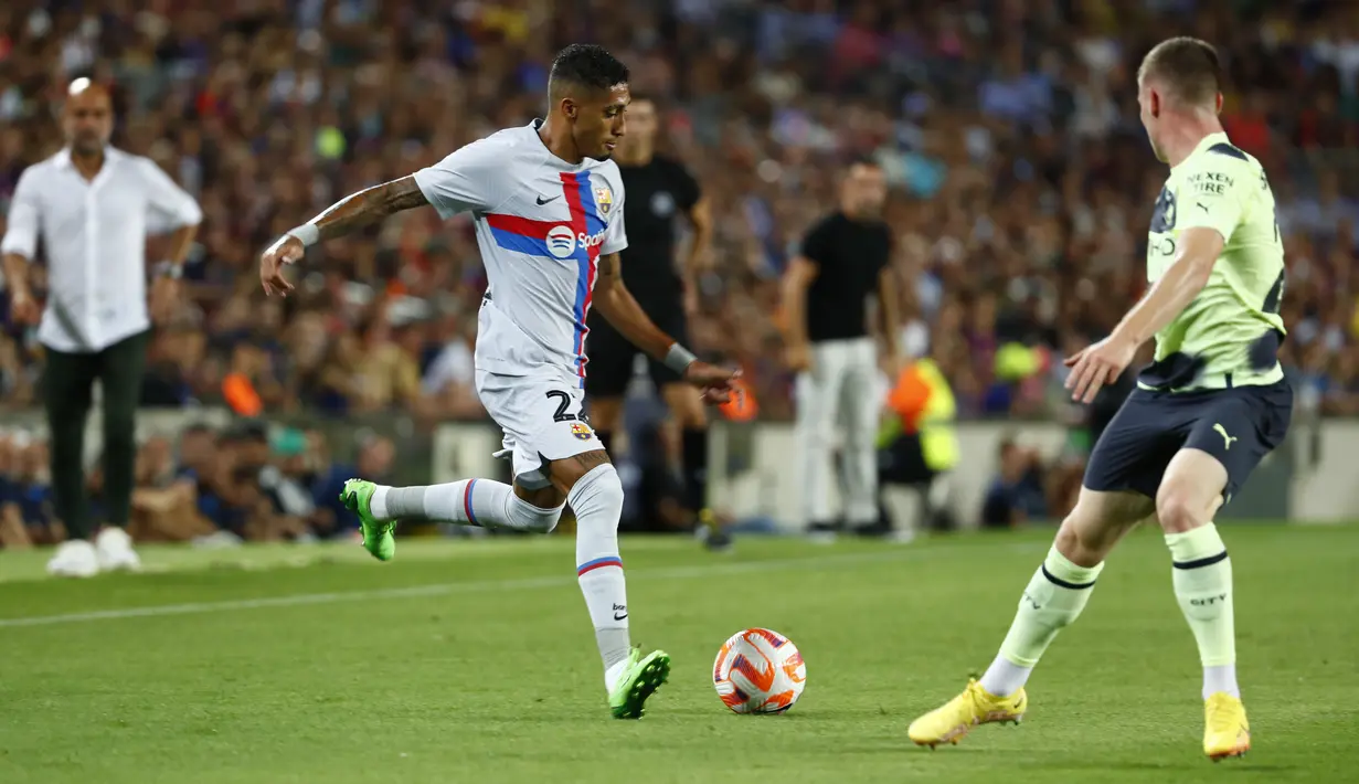 Penyerang Barcelona Raphinha bersaing dengan gelandang Manchester City Sergio Gomez pada sebuah laga amal di Stadion Camp Nou, Kamis (25/8/2022) dini hari WIB. Laga Barcelona vs Man City berjalan ketat, skor akhir sama kuat 3-3. (AP Photo/Joan Monfort)