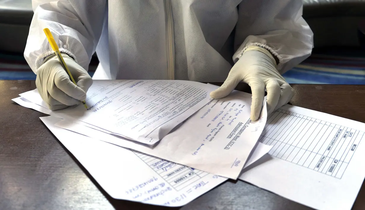 Dokter mengisi formulir untuk tes swab kedua dari fotografer Associated Press Rafiq Maqbool di kamar hotel tempat dia dikarantina, Mumbai, India, 24 April 2020. Setelah dinyatakan negatif, Maqbool diizinkan pulang untuk melakukan karantina di rumah selama 14 hari. (AP Photo/Rafiq Maqbool)