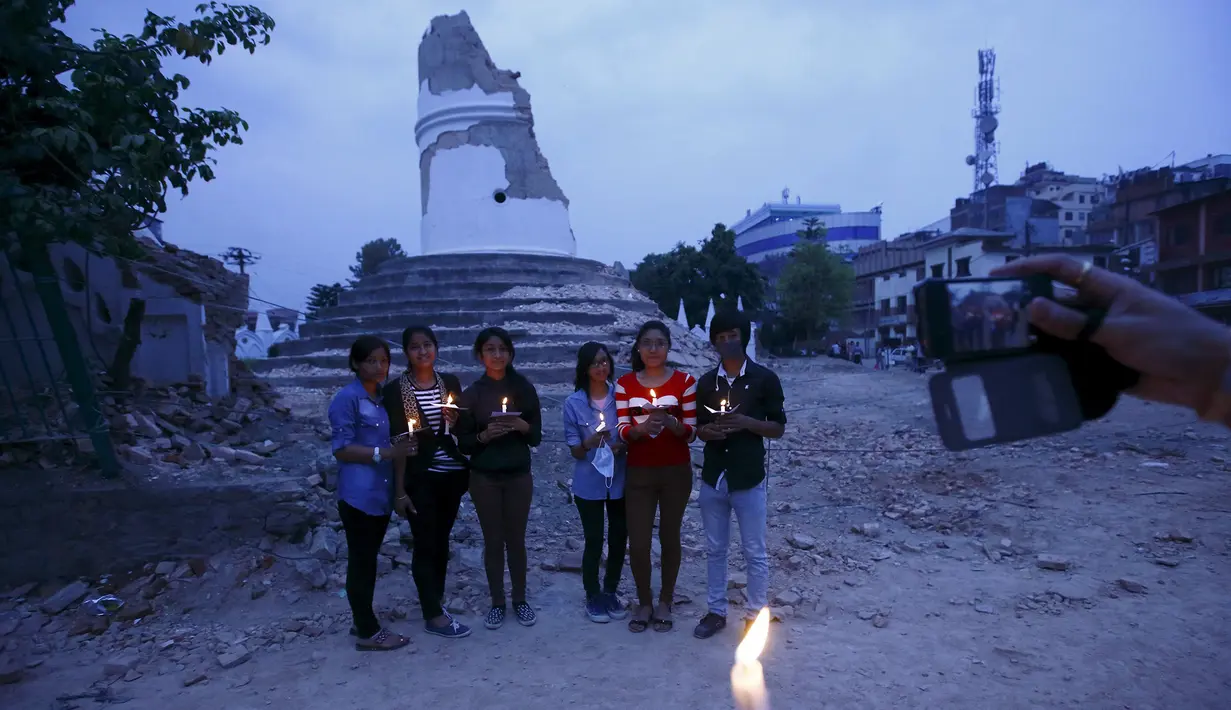 Sejumlah Orang berpose membawa lilin di depan reruntuhan Menara Dharahara untuk menghormati para korban gempa Nepal di Kathmandu, Nepal, (7/5/2015). Gempa berkekuatan 7,8 yang meluluhlantakkan Nepal pada 25 April 2015 lalu. (REUTERS/Navesh Chitrakar)