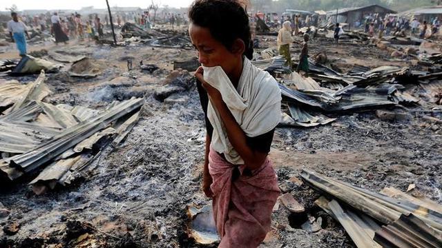 Seorang perempuan berjalan di antara puing-puing kebakaran kamp pengungsi Rohingya di Rakhine pada 3 Mei 2016