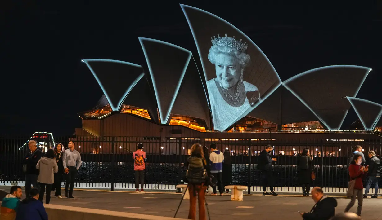 Orang-orang menyaksikan Sydney Opera House diterangi untuk menghormati Ratu Elizabeth II di Sydney, Australia, Jumat (9/9/2022). Sejumlah tempat pun turut menyampaikan duka cita atas meninggalnya sang ratu dengan berbagai cara, mulai dari mematikan lampu pencahayaan hingga mengibarkan bendera setengah tiang. (AP Photo/Mark Baker)