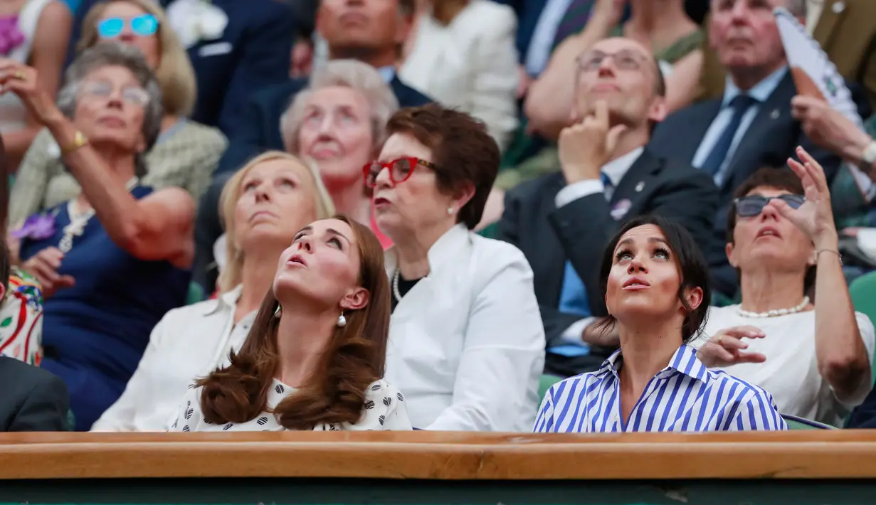 Kate Middleton dan Meghan Markle saat menyaksikan kejuaraan  tenis Wimbledon di London, Inggris, (14/7). Meghan mengenakan kemeja longgar bergaris biru putih serta celana putih. Kate memakai mini dress bermotif hitam putih. (AP Photo/Andrew Couldridge)