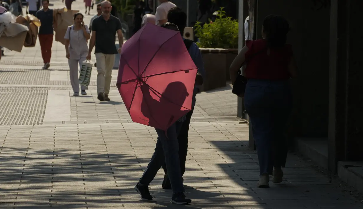 Seorang perempuan berjalan dengan payung untuk melindungi dari matahari di Madrid, Spanyol, Rabu (13/7/2022). Para pakar meteorologi mengatakan massa udara yang terlalu panas dan angin hangat dari Afrika mendorong suhu di kawasan Semenanjung Iberia naik melebihi suhu biasanya. (AP Photo/Paul White)