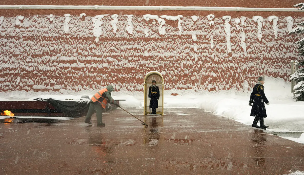 Seorang pekerja membersihkan salju dari Makam Prajurit Tak Dikenal yang dijaga sejumlah prajurit di Tembok Kremlin, Moskow, Rusia, 7 Februari 2022. (AP Photo/Thibault Camus)