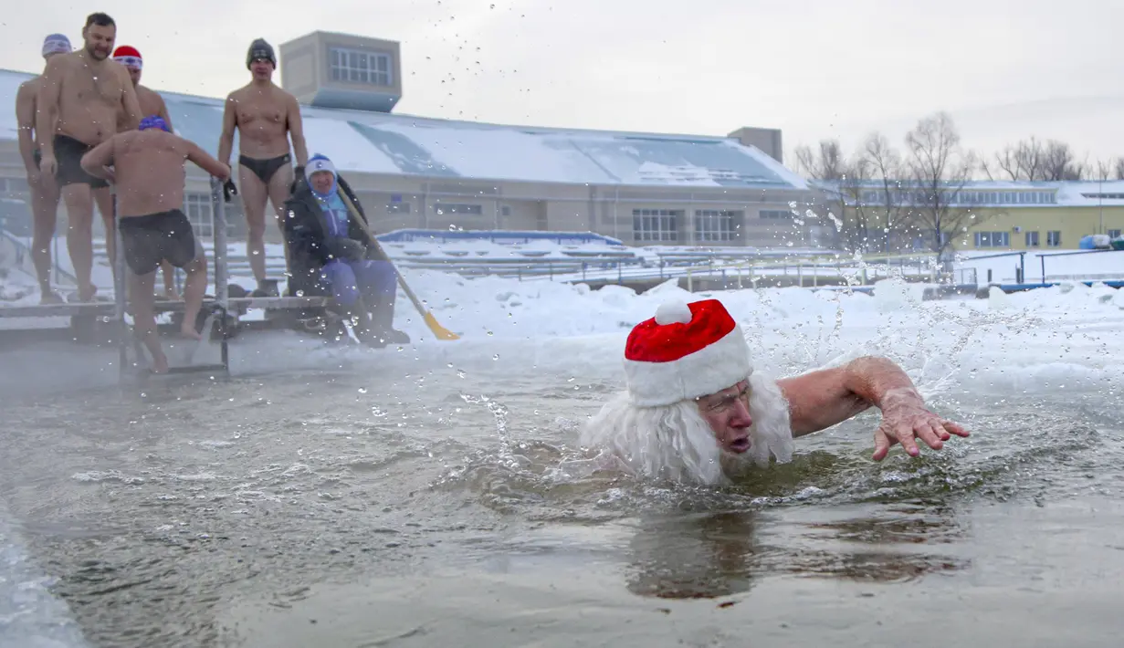 Seorang pria berpakaian seperti Ded Moroz (Santa Claus) berenang di air sedingin es selama hari yang membekukan di kota Omsk di Siberia, Rusia, Sabtu (26/12/2020). Suhu di Omsk turun hingga -32 derajat Celcius atau -25,6 derajat Fahrenheit. (AP Photo/Evgeniy Sofiychuk)