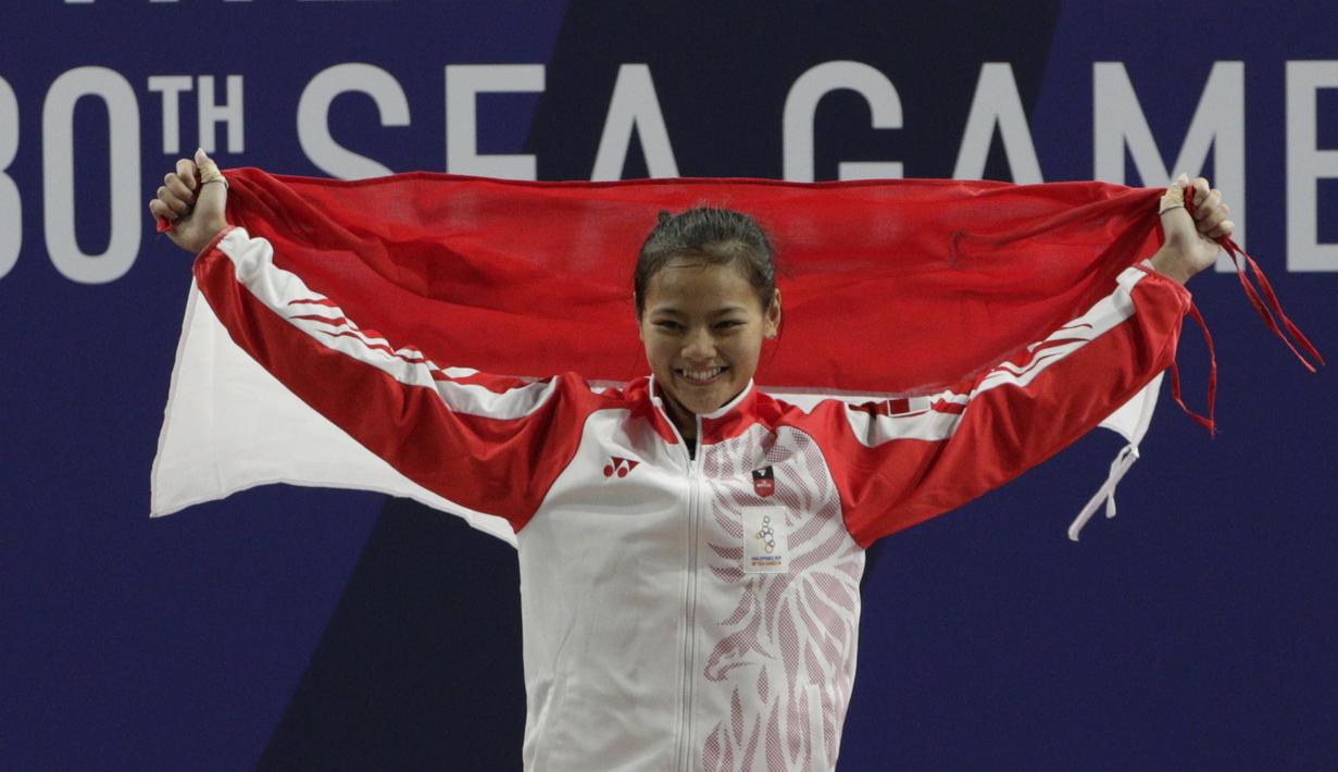 Lifter Aisyah Windy mengibarkan bendera saat naik podium usai mendapatkan medali emas SEA Games 2019 cabang angkat besi nomor 49 kg di Stadion Rizal Memorial, Manila, Minggu (1/12). Dirinya meraih emas dengan total angkatan 104 kg. (Bola.com/M Iqbal Ichsa