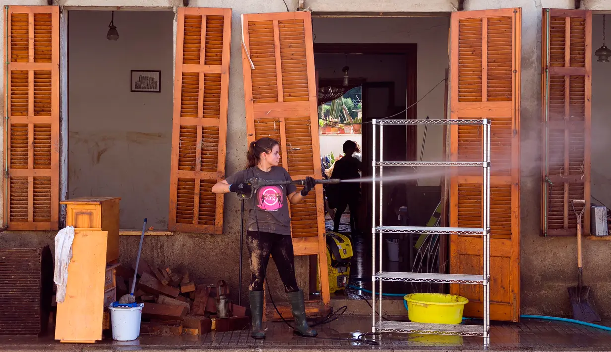 Seorang wanita membersihkan rumahnya yang terkena banjir bandang di Sant Llorenc, Mallorca, Spanyol (11/10). Banjir bandang tersebut telah menewaskan setidaknya 10 orang. (AP Photo/Francisco Ubilla)
