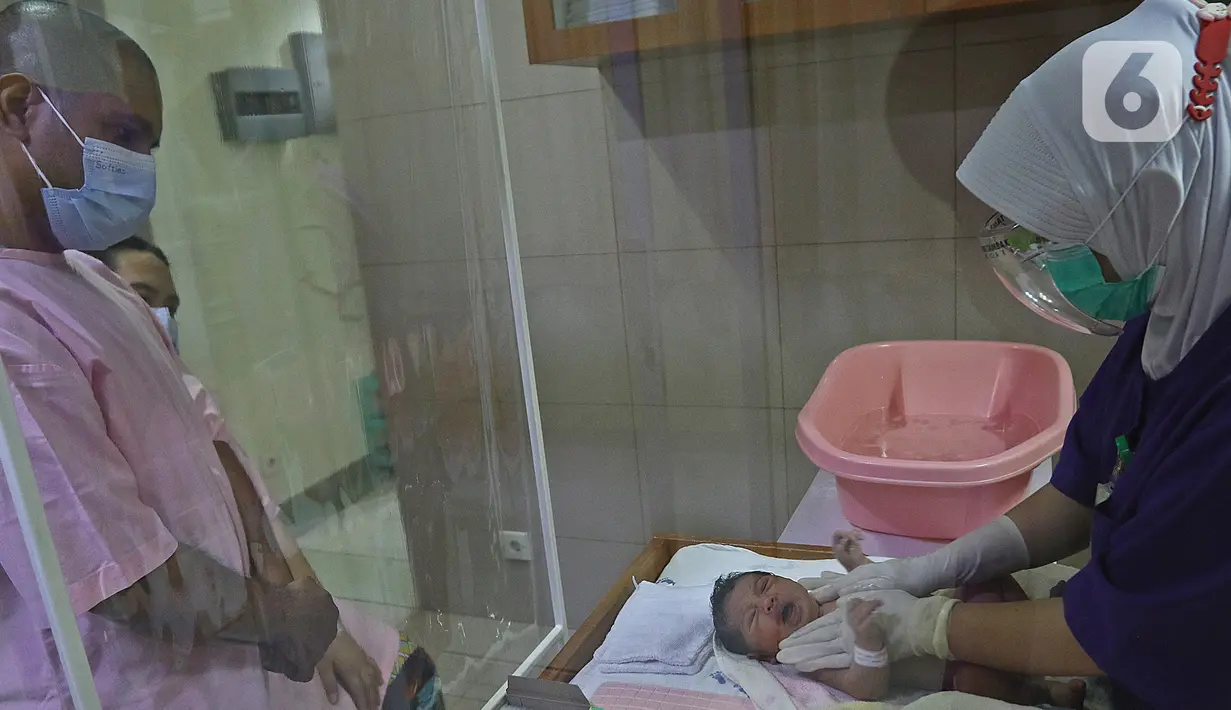 Pasangan orangtua baru memperhatikan saat perawat mempraktekan cara memandikan bayi di RSIA Tambak, Jakarta, Kamis (18/02/2021). Melatih para ibu baru untuk memandikan bayi pertama tersebut dilakukan dengan menerapkan protokol kesehatan ketat. (Liputan6.com/Herman Zakharia)