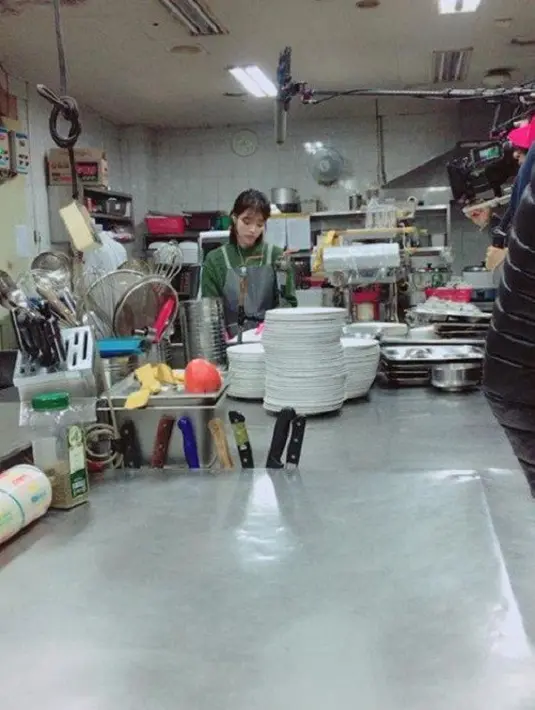 Dalam sebuah gambar, IU terlihat sedang berada di dapur yang bisa menjadi restoran. (Foto: Allkpop.com)