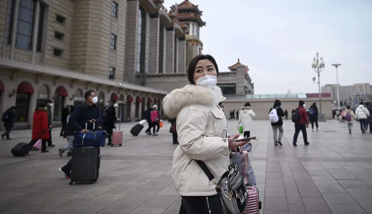 Seorang wanita melihat ke belakang saat dia berjalan ke pintu masuk stasiun kereta api Beijing di ibu kota China (7/1/2023). Ketika migrasi tahunan dimulai dengan orang-orang yang kembali ke kampung halaman mereka untuk perayaan Tahun Baru Imlek. (AFP/Wang Zhao)