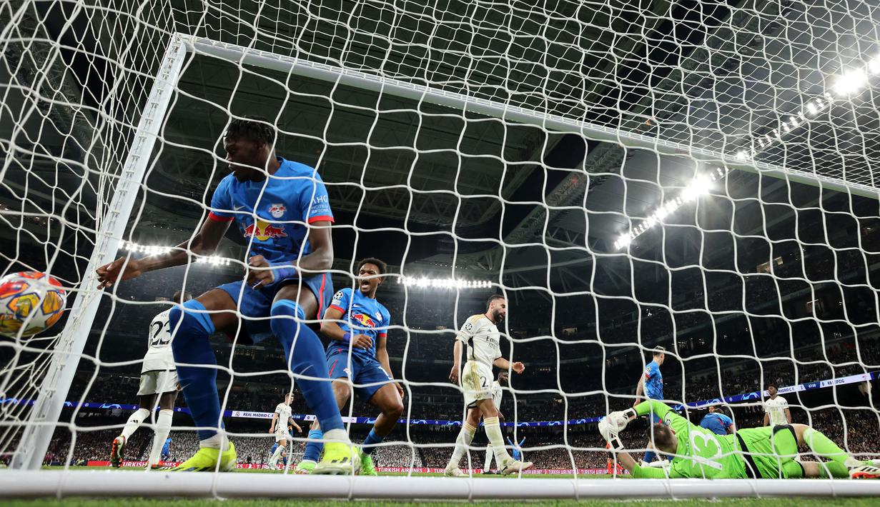 Kiper Real Madrid, Andriy Lunin (kanan) gagal menghalau bola yang berakibat gol untuk RB Leipzig pada laga leg kedua 16 besar Liga Champions 2023/2024 di Santiago Bernabeu, Madrid, Spanyol, Kamis (07/03/2024) WIB. (AFP/Pierre-Philippe Marcou)