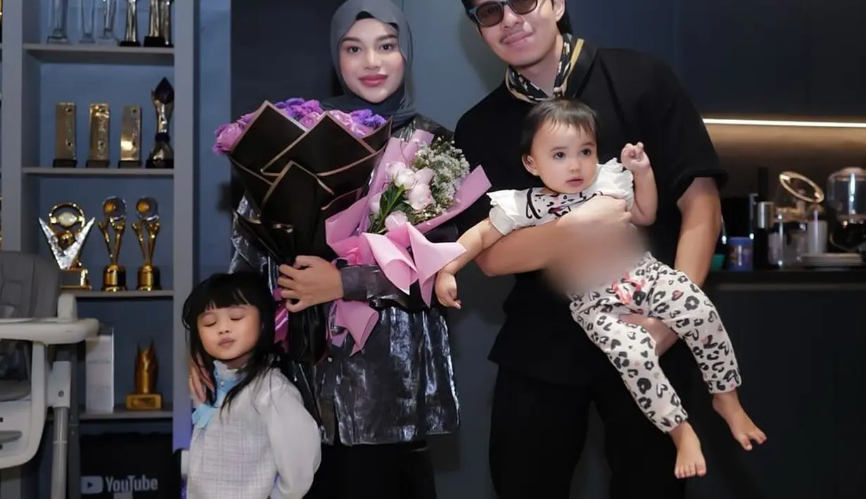 Dapat buket bunga dari sang suami, Aurel Hermansyah tampil anggun dengan tunik dan maxi skirt hitam. Penampilannya dilengkapi dengan hijab segi empat warna dark grey. Begitu juga Atta yang tampil serasi dengan setelan hitam-nya. [@aurelie.hermansyah].
