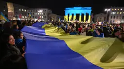 Orang-orang mengambil bagian dalam unjuk rasa pro-Ukraina di depan Gerbang Brandenburg, yang diterangi dengan warna-warna bendera Ukraina, menandai tiga tahun invasi Rusia ke Ukraina di Berlin pada 24 Februari 2025. (RALF HIRSCHBERGER/AFP)