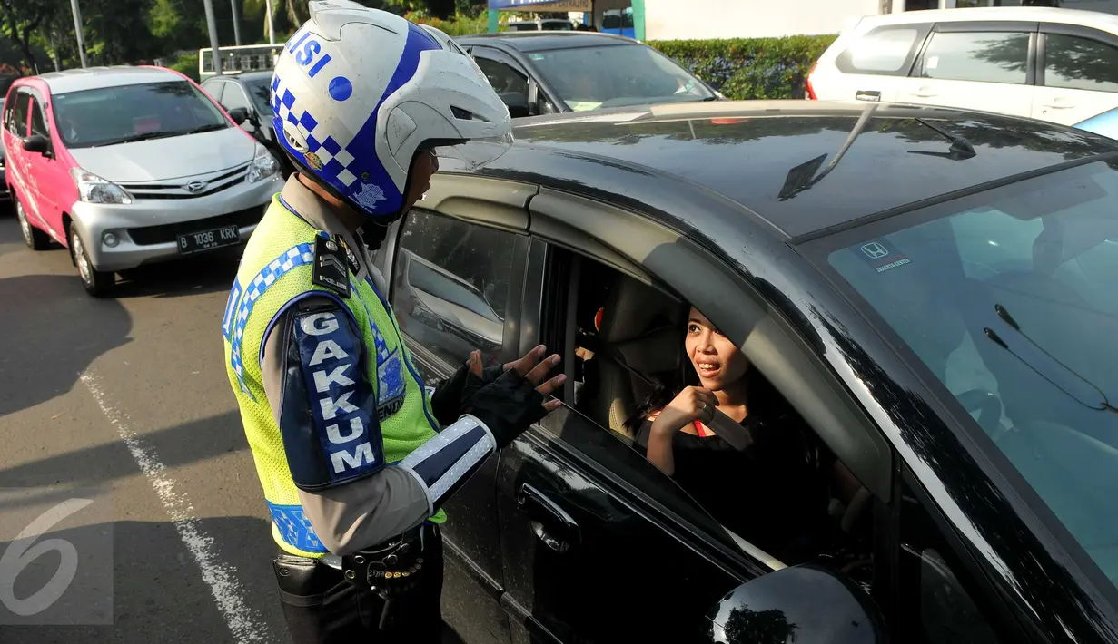 Petugas kepolisian memberikan informasi kepada pengendara mobil terkait penerapan sistem ganjil genap di Bundaran Senayan, Jakarta, Rabu (27/7). Penerapan ganjil genap yang dimulai pada hari ini masih tahap uji coba. (Liputan6.com/Gempur M Surya)