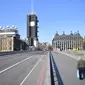 Sebuah gambar menunjukkan Gedung Parlemen (kiri) di ujung Westminster Bridge yang kosong dengan seorang pejalan kaki di trotoar London setelah pemerintah Inggris setempat memberlakukan lockdown akibat pandemi Covid-19 pada 24 Maret 2020. (Photo by JUSTIN TALLIS / AFP)