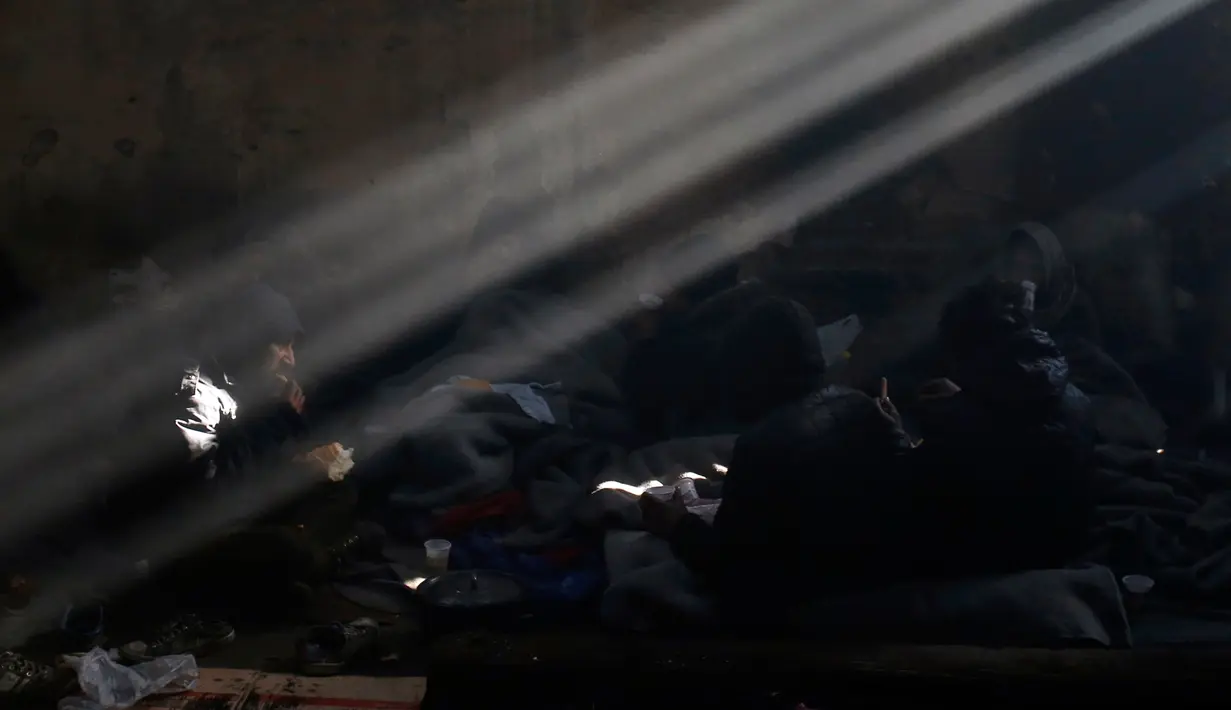 Sejumlah imigran menikmati makanannya usai mengantre panjang di sebuah gudang kosong di Belgrade, Serbia (8/1). Mereka hanya mengandalkan makanan dari bantuan dan tempat tinggal seadanya untuk bertahan hidup di salju dingin. (AP Photo/Darko Vojinovic)