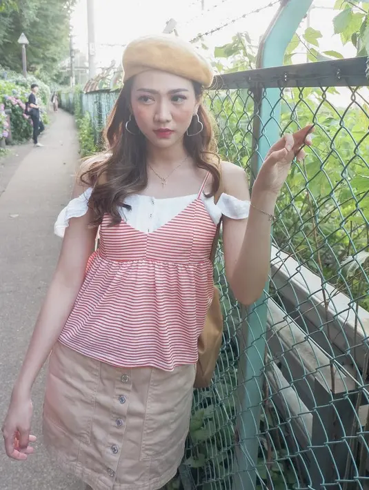 Perempuan kelahiran 1998 ini juga mengenakan off shoulder top putih dengan outer spaghetti strap bergaris merah, dipadu dengan mini skirt cokelatnya. Ia mengenakan topi baret warna cokelat sebagai pelengkap penampilan. @shanju.