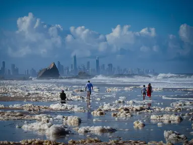 Turis berjalan di antara busa tebal setelah siklon tropis di Pantai Currumbin, Gold Coast, Australia pada 15 Desember 2020. Hujan lebat dan angin kencang telah melanda kawasan perbatasan padat penduduk antara New South Wales dan Queensland selama tiga hari. (Photo by Patrick HAMILTON / AFP)