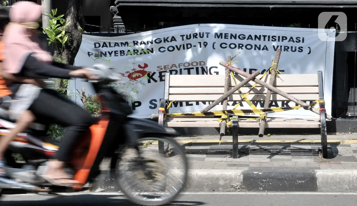 Pengendara melintasi bangku trotoar yang disegel garis pembatas dan ditutupi bambu di kawasan Rawamangun, Jakarta, Minggu (3/5/2020). Bangku trotoar di sepanjang jalan Rawamangun disegel untuk mencegah kerumunan warga sebagai upaya memutus rantai penyebaran COVID-19. (merdeka.com/Iqbal S. Nugroho)