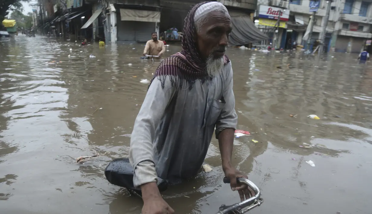 Seorang pria membawa sepeda menyeberangi jalan yang banjir setelah hujan deras di Lahore, Pakistan (16/7/2019). Di Kashmir yang dikelola Pakistan, para pejabat pemerintah mengatakan sedikitnya 23 orang tewas setelah hujan lebat memicu banjir bandang. (AP Photo/K.M. Chaudary)