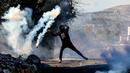 Seorang pemuda Palestina menggunakan ketapel untuk mengembalikan tabung gas air mata ke arah pasukan keamanan Israel saat bentrok pada demonstrasi menentang pengambilalihan tanah oleh Israel dekat pemukiman Yahudi Kedumim di Desa Kfar Qaddum, Tepi Barat, 21 Januari 2022. (JAAFAR ASHTIYEH/AFP)