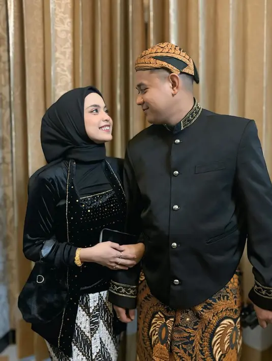 Pedangdut berusia 20 tahun itu tampil elegan dengan kebaya hitamnya, beserta hijab warna senada. Sementara itu, sang suami tampil gagah kenakan beskap dan blangkon. Keduanya tetap serasi dengan perpaduan bawahan kain batik, meski berbeda motif. (Liputan6.com/IG/@putriisnari3)