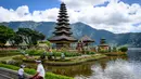 Berlatar belakang perbukitan serta pegunungan yang hijau menambah nilai estetika panorama pura ini. Tampak dalam foto, seorang pria duduk di depan Pura Ulun Danu Beratan, sebuah pura Hindu di Danau Beratan dekat Bedugul, Bali, pada Jumat 7 November 2025. (Mladen ANTONOV/AFP)