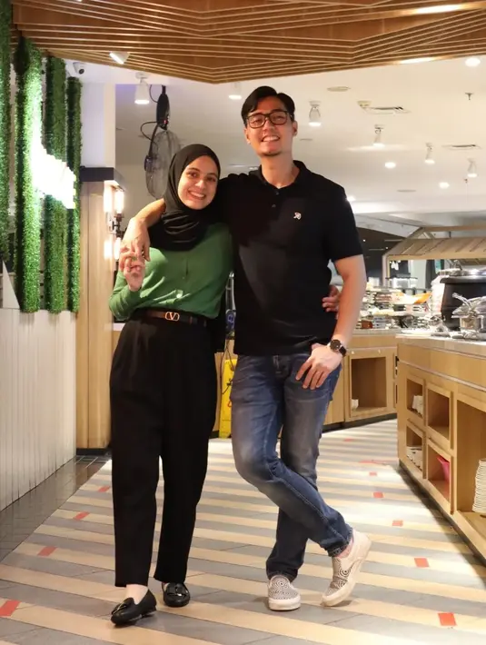 Berpose berdua bersama sang suami, Nycta Gina tampil mengenakan atasan berwarna hijau. Ia memadukan penampilannya dengan celana panjang hitam, dan hijab pashmina yang juga berwarna hitam. Foto: Instagram.