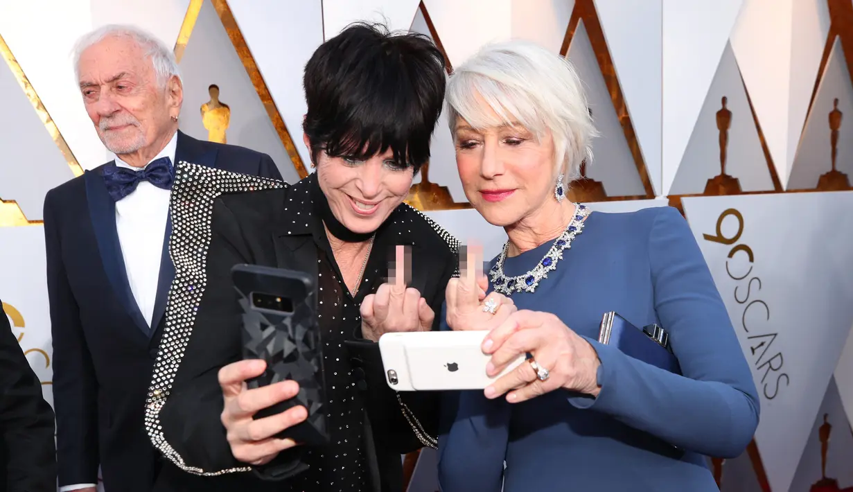 Aktris senior Helen Mirren melakukan wefie dengan sahabat sekaligus penyanyi Diane Warren di karpet merah Piala Oscar 2018, Los Angeles, Minggu (4/3). Acungan jari tengahnya tersebut menjadi perbincangan di internet. (Christopher Polk/GETTY IMAGES/AFP)