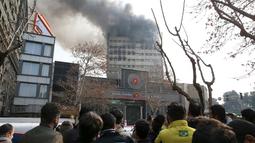 Warga menyaksikan kebakaran yang melanda gedung pencakar langit tertua Iran, gedung Plasco berlantai 15 di pusat kota Teheran, Kamis (19/1). Beberapa bagian bangunan runtuh di tengah upaya pemadam kebakaran menjinakkan api. (AP Photo/Vahid Salemi)