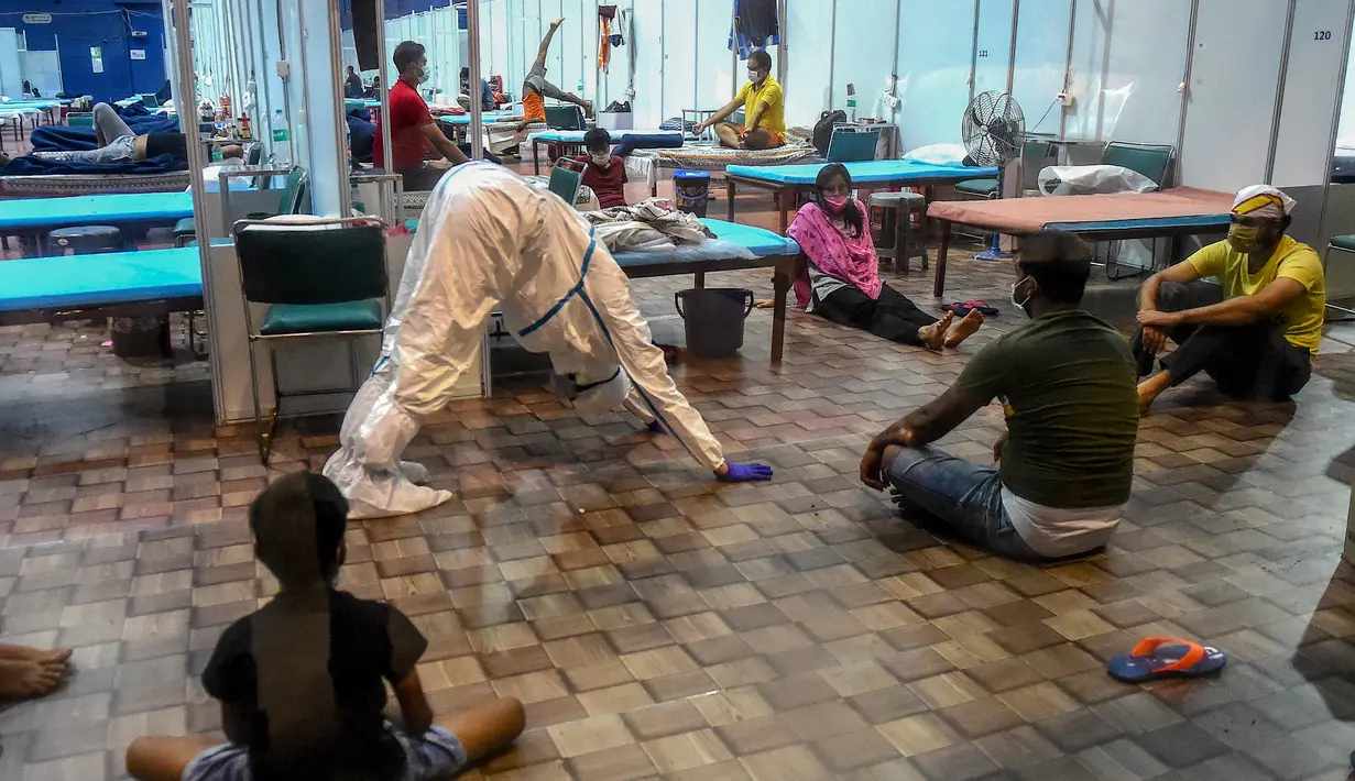 Seorang dokter yang mengenakan setelan Alat Pelindung Diri memberikan instruksi kepada pasien saat melakukan yoga di dalam bangsal di kompleks olahraga Commonwealth Games (CWG) Village yang sementara diubah menjadi pusat perawatan Covid-19 di New Delhi, India, Kamis (16/7/2020). (Money SHARMA / AFP)