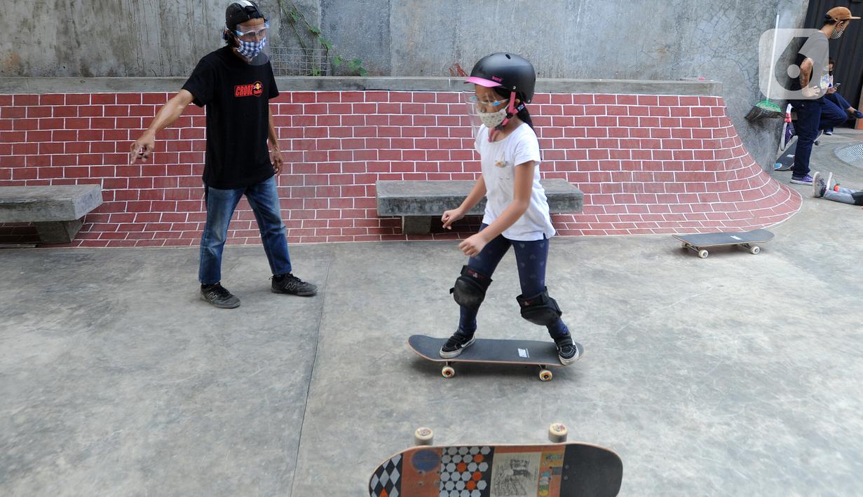 Instruktur melatih seorang anak menggunakan skateboard dengan memakai masker dan face shield di Crooz Shophouse di kawasan Duren Tiga, Jakarta Selatan, Minggu (2/8/2020). Mereka kembali melakukan latihan seminggu dua kali dengan menerapkan protokol kesehatan. (merdeka.com/Arie Basuki)