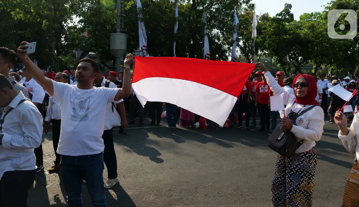 Relawan Joko Widodo-Ma'ruf Amin mengibarkan bendera Merah Putih saat nonton bareng pelantikan Presiden dan Wakil Presiden di Taman Aspirasi, Jakarta, Minggu (20/10/2019). Jokowi dan Ma'ruf Amin resmi dilantik sebagai Presiden dan Wakil Presiden RI periode 2019-2024. (Liputan6.com/Herman Zakharia)