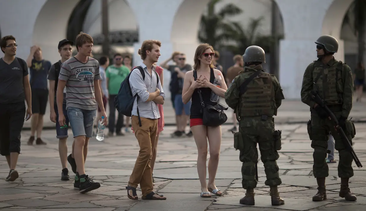 Wisatawan berbincang dengan tentara saat mereka berpatroli di lingkungan Lapa di Rio de Janeiro, Brasil, (30/7). Ribuan tentara mulai berpatroli di Rio de Janeiro di tengah lonjakan kekerasan di kota terbesar kedua di Brasil. (AP Photo / Leo Correa)